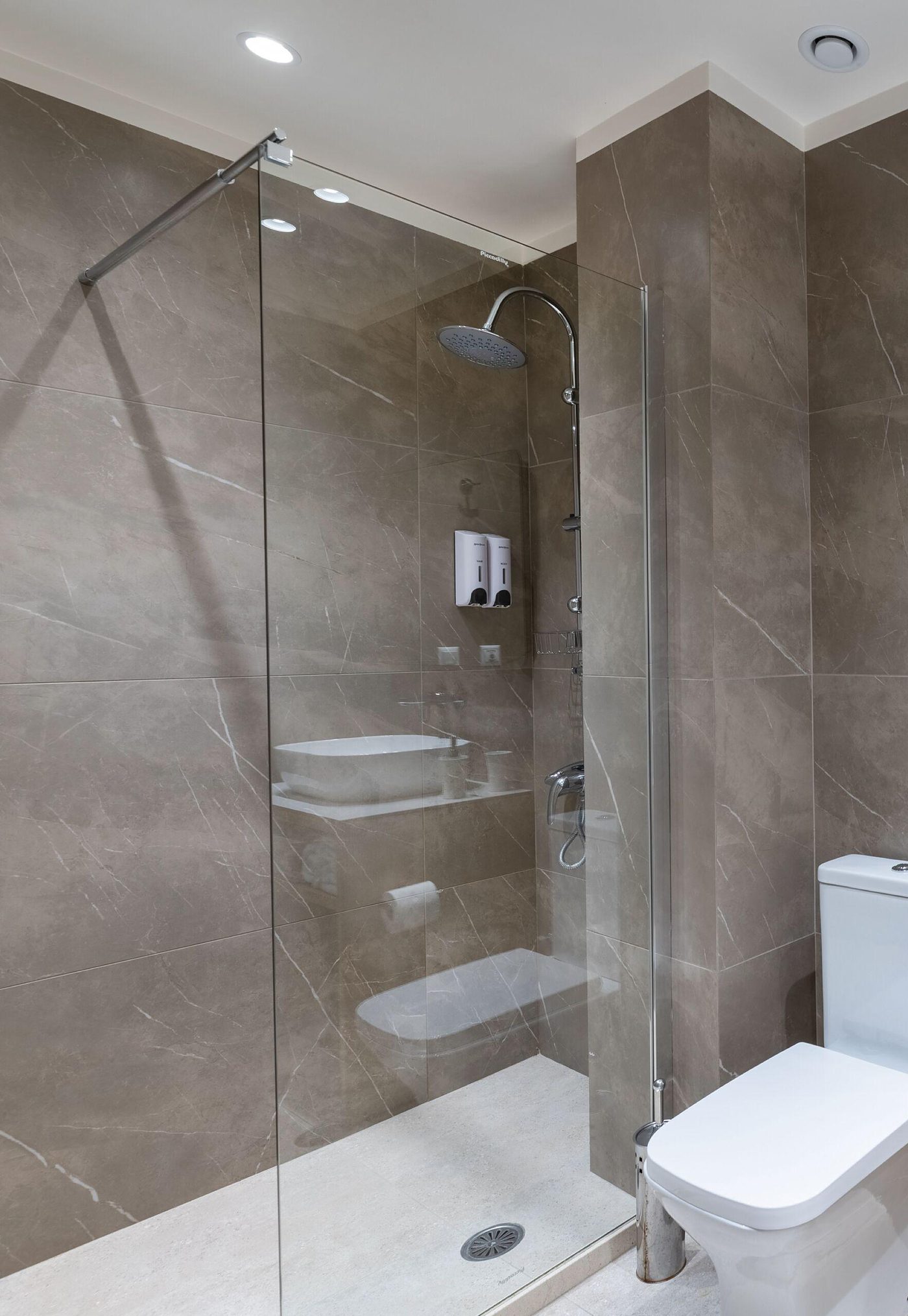 Glass shower and stone tiled bathroom with towels on an oak stand